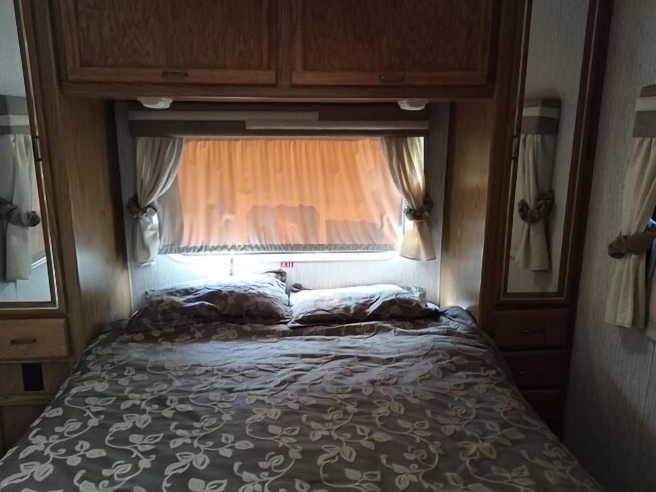 Ein Schlafzimmer mit Bett, Vorhängen, einem Fenster und Holzschränken.