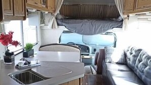 Een compact RV-interieur met een kitchenette, een bed en een zithoek.