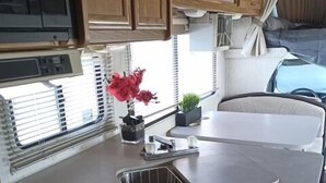 Een kleine keuken met een gasfornuis, houten kastjes, een spoelbak en een raam met jaloezieën.