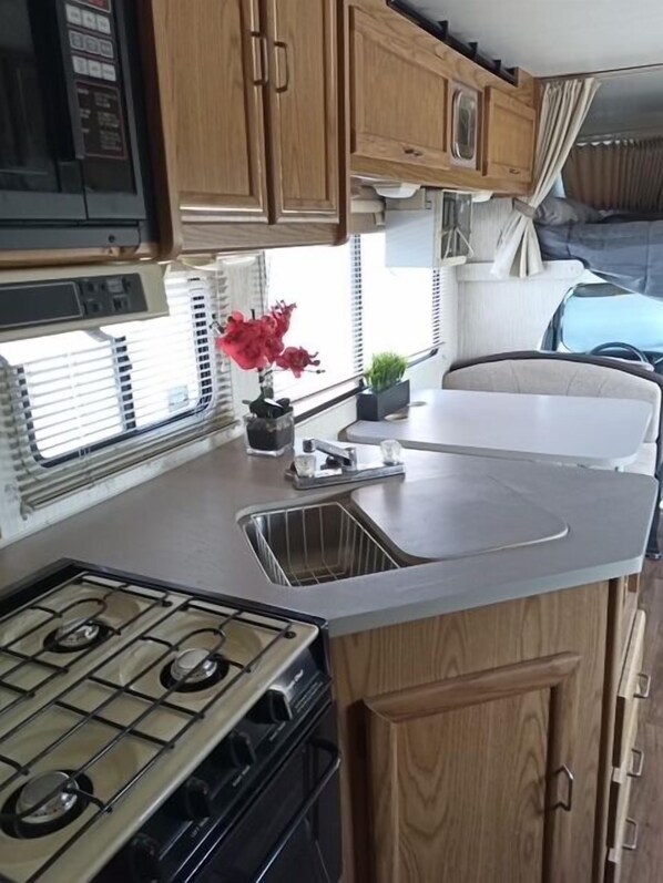 A compact kitchen with a gas stove, wooden cabinets, a sink, and a window with blinds.