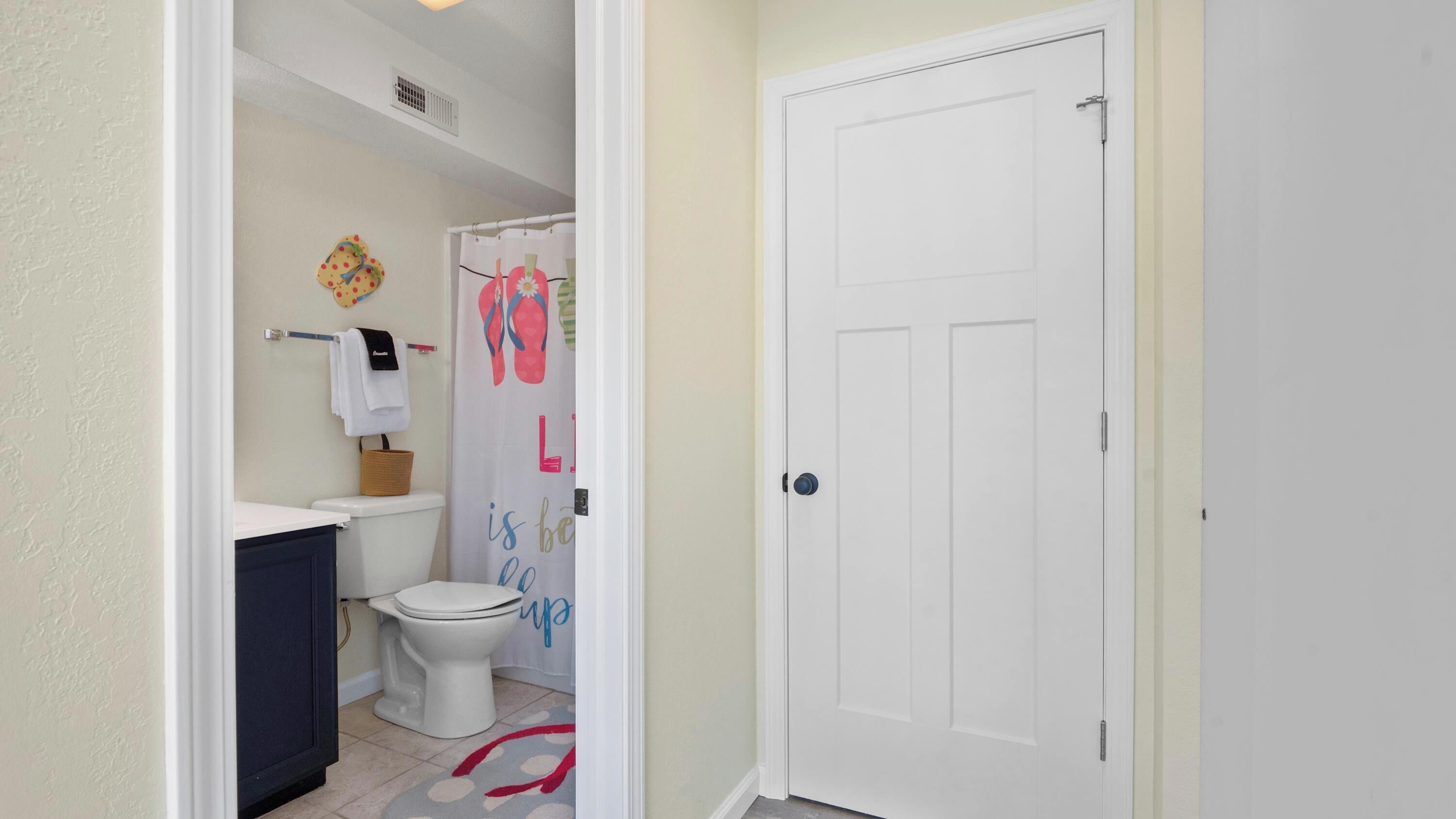 A bathroom with a toilet, a small sink, a shower curtain with flip-flop designs, and a white door.