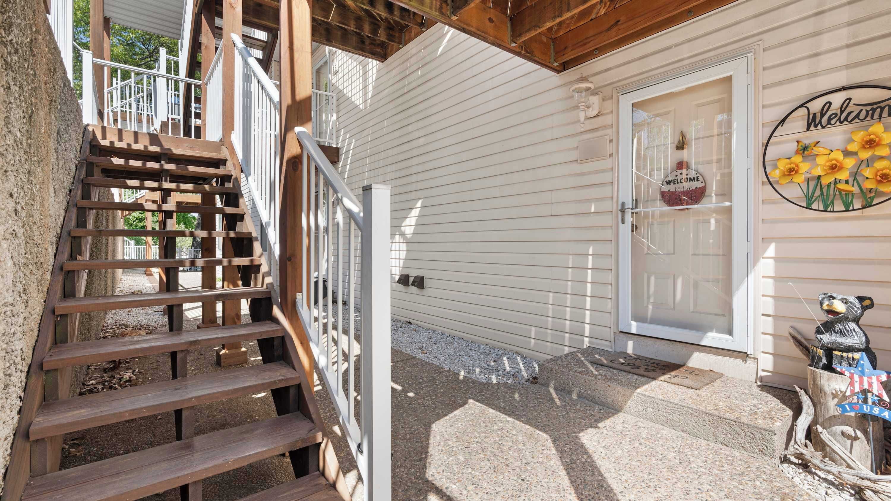 A wooden staircase leading to a white building with a 'Welcome' sign and a bear statue outside.