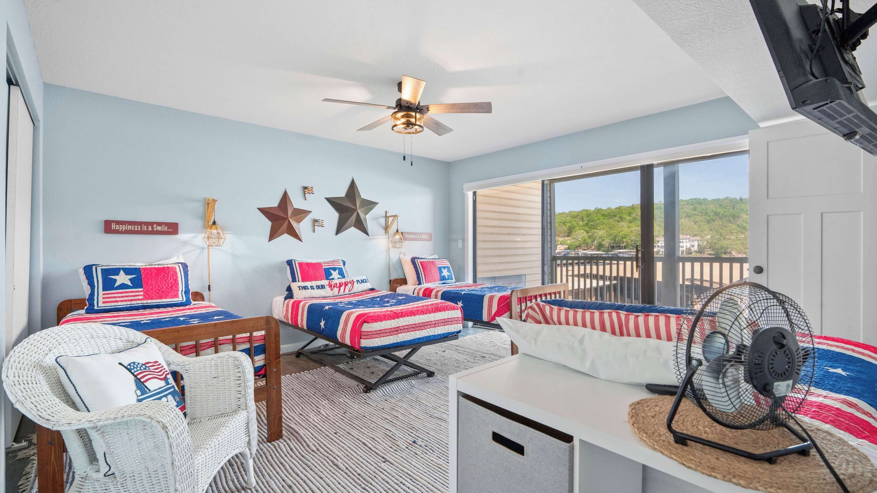 A bedroom with two beds, a ceiling fan, a large window, and a balcony.