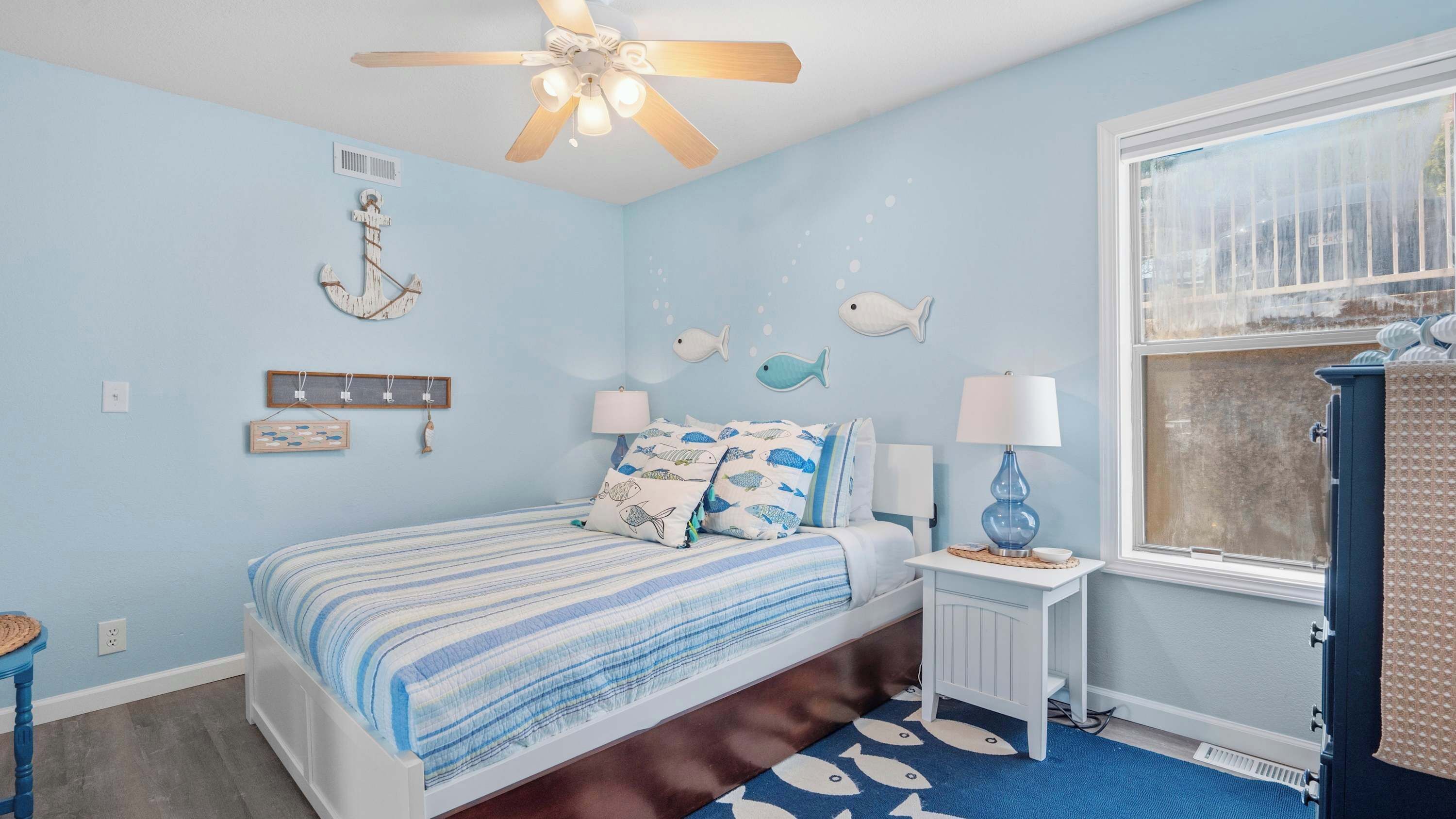 A bedroom with a bed, a ceiling fan, a window, and wall decorations.