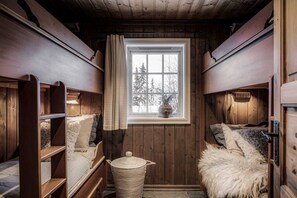 A cabin with wooden walls, a window with a view of trees, bunk beds, and a woven basket.