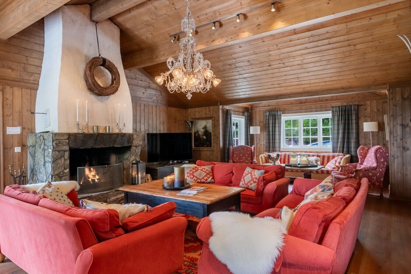 A cozy living room with a fireplace, red sofas, a chandelier, and a stone fireplace surround.