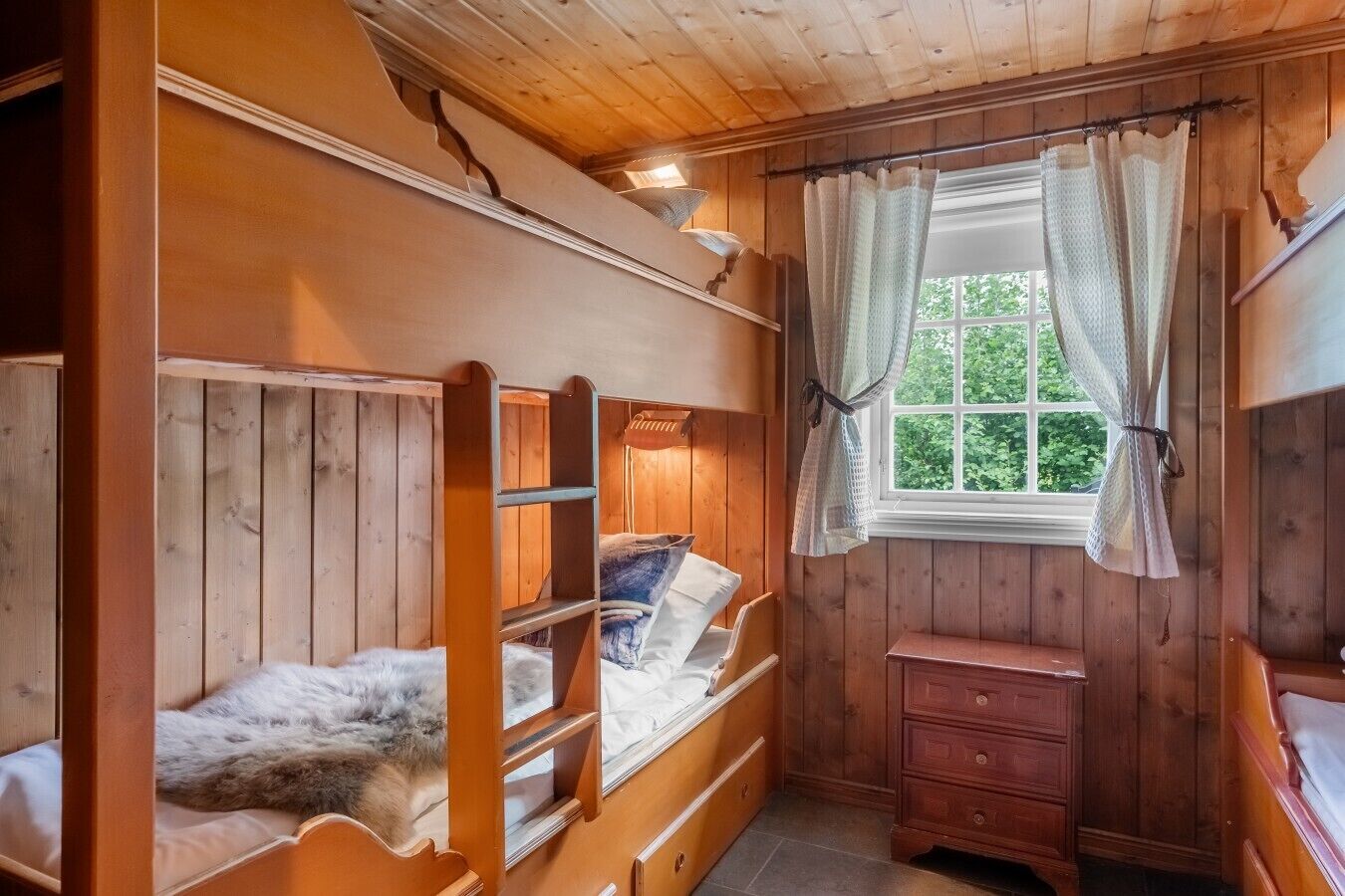 Une chambre de style cabane avec des lits superposés, une petite commode et une fenêtre avec des rideaux.