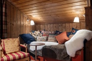 A cozy cabin interior with a wooden ceiling, a sofa with patterned cushions, a chair, and a small round table.