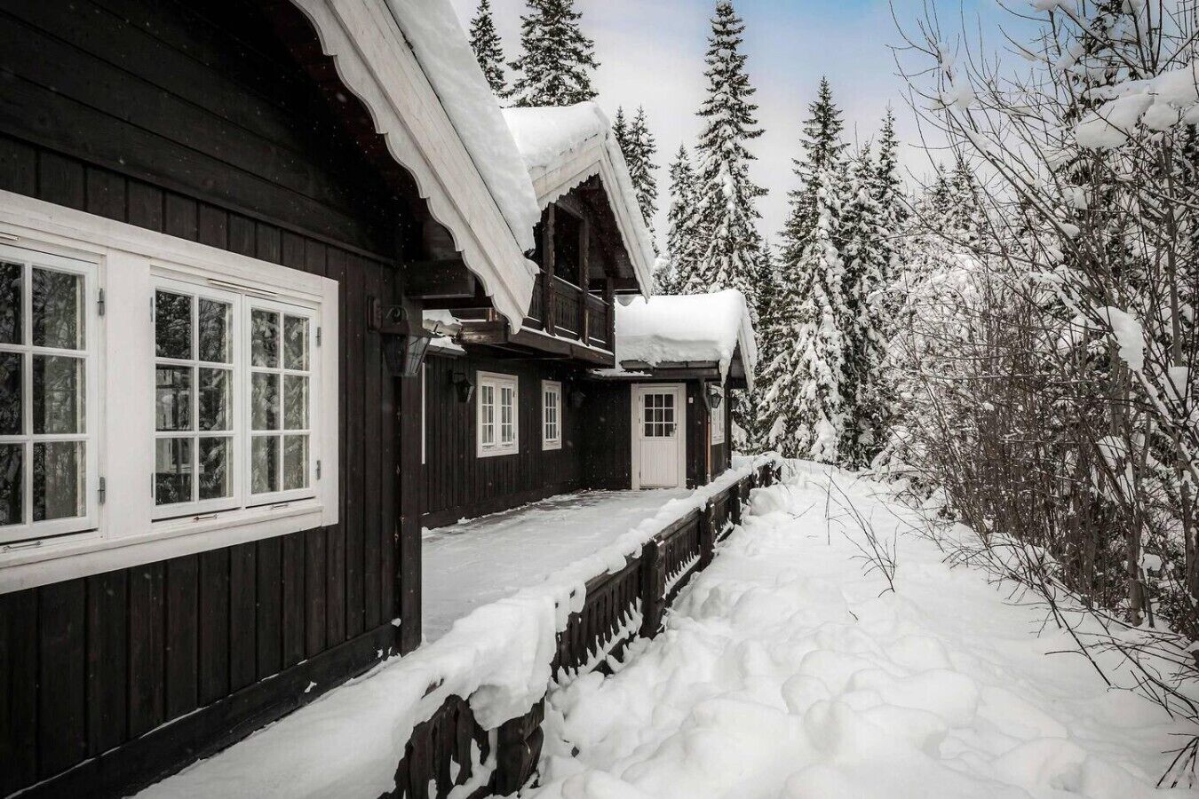 En stuga av trä med en veranda, omgiven av snötäckta träd.