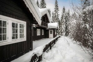 A wooden cabin with a porch, surrounded by snow-covered trees.