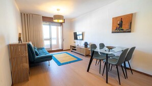 A modern living room with a sofa, dining table, chairs, a TV, and a painting on the wall. - Modern & Versatile Urban Refuge - APT Antas (Porto Antas)