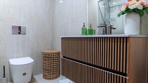Casa de banho moderna com sanita, bidé e toucador de madeira com espelho.