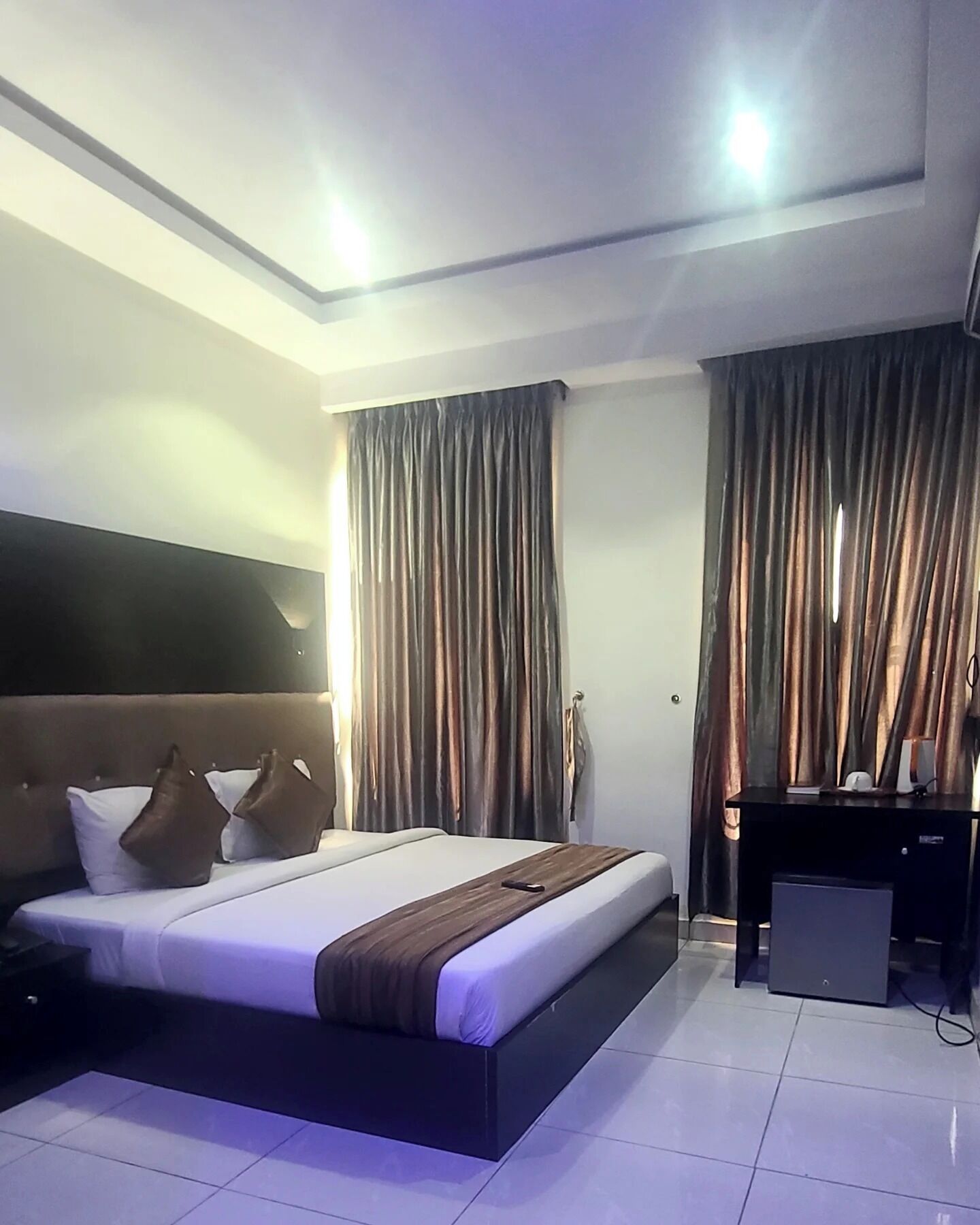 Ein Hotelzimmer mit Bett, Vorhängen, Schreibtisch und Fernseher.