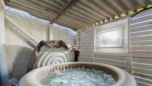 Un jacuzzi en una habitación rústica con techo de madera y ventana con persianas.