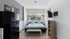 Una habitación compacta con cama, un banco, televisor y refrigerador.