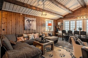 A cozy living room with a wooden ceiling, a large sofa, a coffee table, and a dining area with chairs. - TH589 Ski-in/Out Cabin, Sauna, 13 Guests (Trysil)