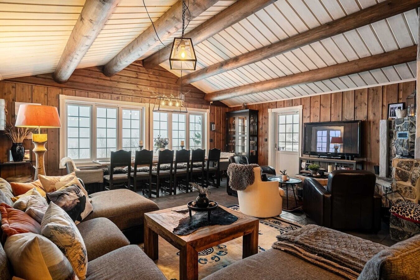 L’intérieur chaleureux d’un chalet en bois comprend un coin repas, des sièges, un téléviseur et une cheminée.
