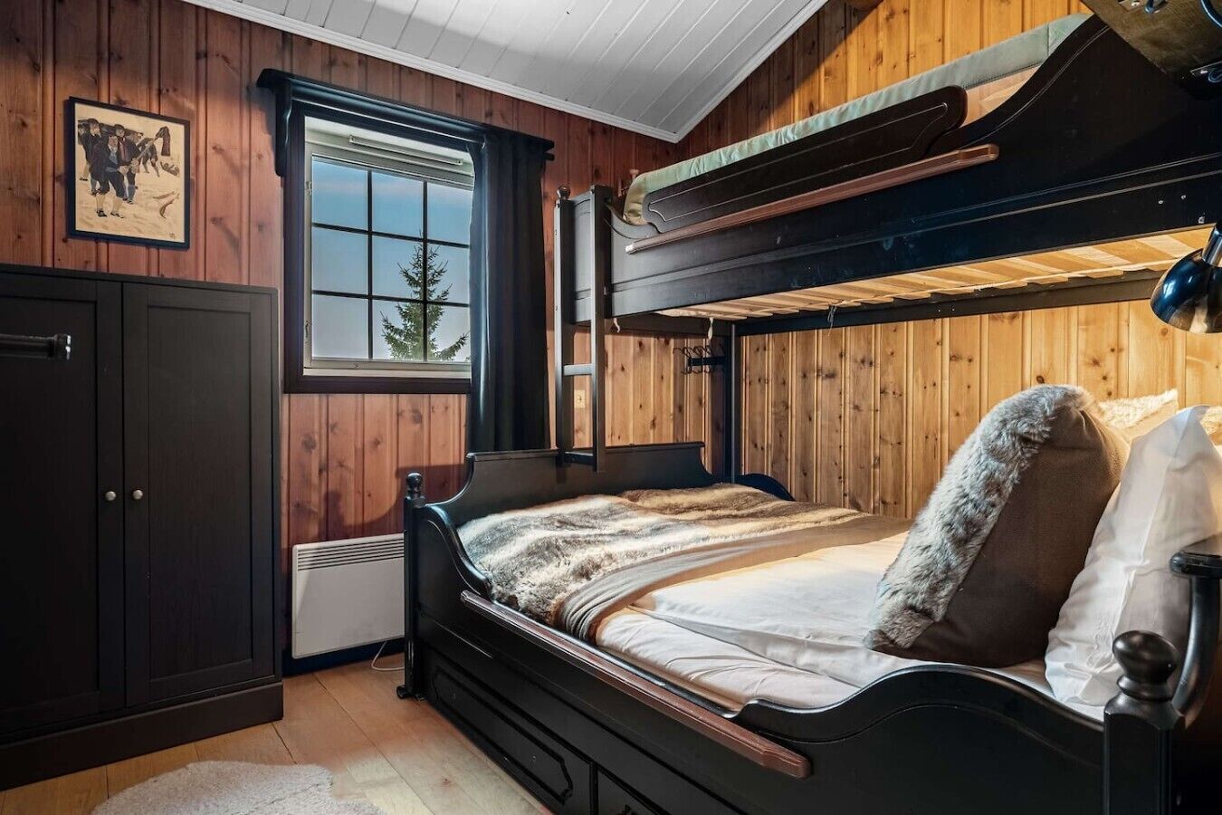 A bunk bed with a headboard, a window with curtains, a wooden wall, and a framed picture.