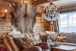A log cabin interior with a fur rug, leather sofa, chandelier, and a view through a window. - TH587- Premium Ski-inout Chalet, 4 Bed, 4 Bath (Trysil)