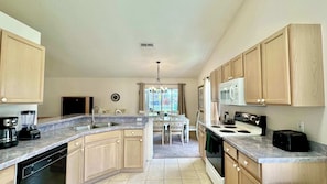 A kitchen with a central island, a dining table, wooden cabinets, a microwave, stove, and a dishwasher. - Sunlit Splash Private Pool (Kissimmee)