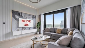 Un salon moderne avec un canapé, une table basse, un téléviseur fixé au mur et une grande fenêtre.