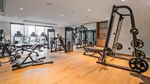 Une salle de sport équipée de divers appareils d’exercice, dotée de grandes fenêtres et d’un plancher en bois.