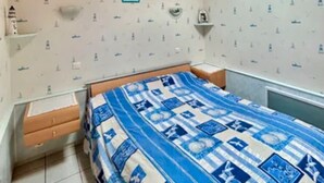 A bedroom with a wooden ceiling, a skylight, a bed with a blue and white quilt, and patterned wallpaper. - Vacation home in Andernos-les-Bains - Sleeps 6 - Near beach and market (Andernos-les-Bains)