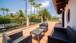Um terraço ao ar livre com móveis de vime, piscina e palmeiras.