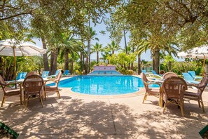 A pool area with lounge chairs and umbrellas, surrounded by palm trees. - Can Tirenet accommodate 8 people Wi-Fi, swimming pool, tennis/padel (Alcudia)