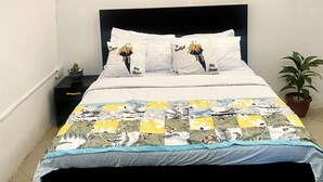 Camera da letto con un letto, cuscini decorati con motivi floreali, un comodino con una pianta e un'opera d'arte raffigurante figure africane e una mappa.