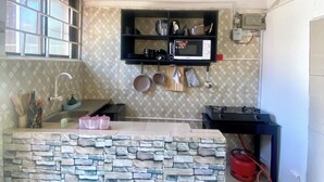 Una cucina compatta con rivestimento in pietra, una mensola a incasso con pentole e utensili, un forno a microonde e un piano cottura a gas.