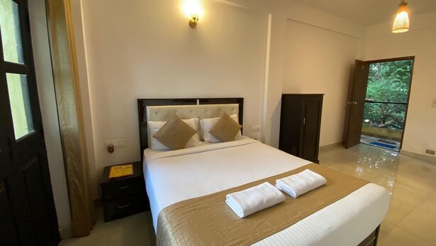 A hotel room with a large bed, a bedside table, a wardrobe, and a view of the outdoors. - GFV Stays (Candolim)