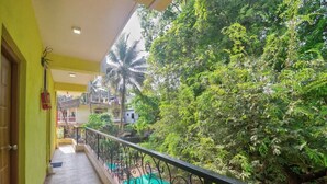 A balcony with a view of lush greenery and a building in the background. - GFV Stays (Candolim)