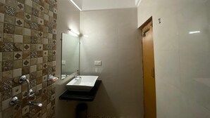 A bathroom with a tiled wall, a sink, a mirror, and a shower. - GFV Stays (Candolim)