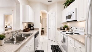 A modern kitchen with white cabinetry, stainless steel appliances, and a central island with a sink. - Universal Palms Retreat at Windsor Palms (Kissimmee)