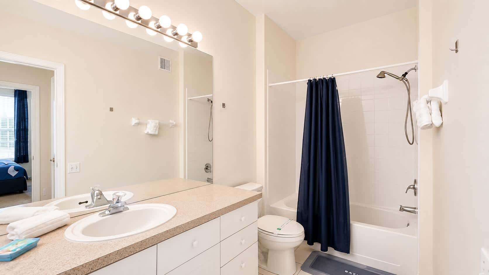 A bathroom with a double sink, a mirror with lights, a shower, and a toilet.