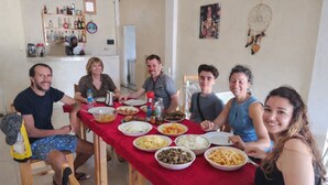 A group of people seated around a table with various dishes, in a room with a tiled floor and a shelf with bottles in the background. - Azure Flat Casa Carlotta -100 mt from the Beach, Cozy and Authentic (Vila do Maio)