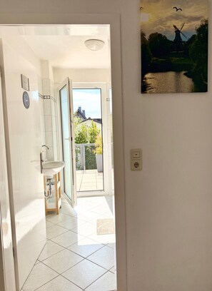Une salle de bain avec un lavabo, un miroir et une vue sur une maison et un moulin à vent, visibles à travers une porte ouverte.