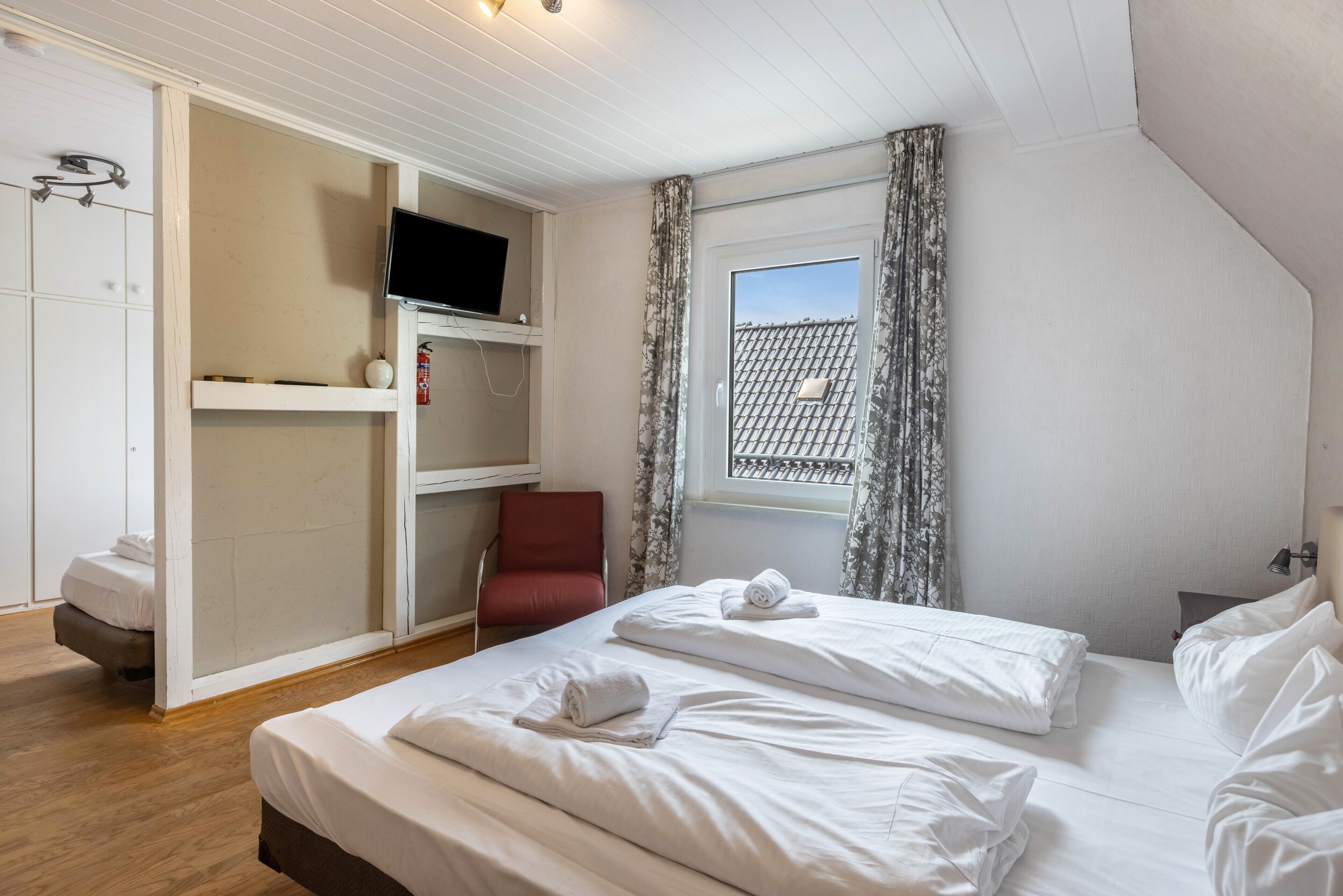 Een slaapkamer met twee bedden, een televisie, een kledingkast, een stoel en een raam met gordijnen.