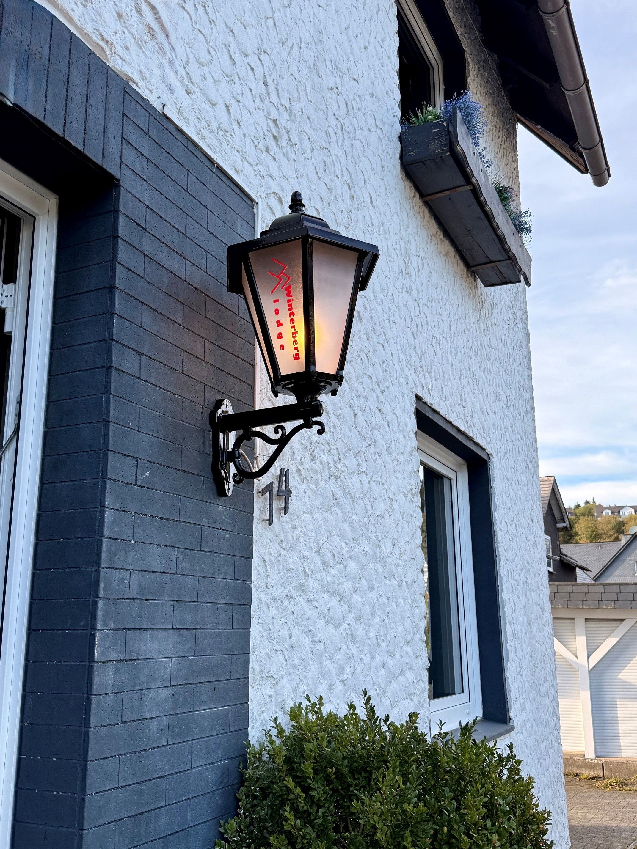 A building with a black brick facade, a white textured wall, and a black street lamp with 'Winterberg Lodge' written on it.