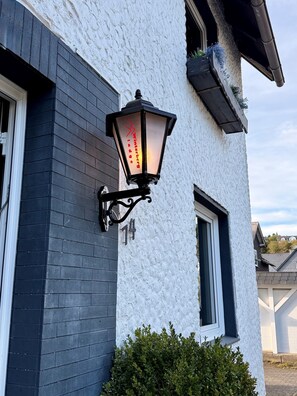 Un bâtiment à la façade en briques noires, avec un mur blanc à la texture particulière, et un lampadaire noir sur lequel on peut lire l’inscription « Winterberg Lodge ».