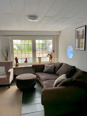Una sala de estar con un sofá modular, un otoman redondo, un sillón blanco y una mesita con objetos decorativos.