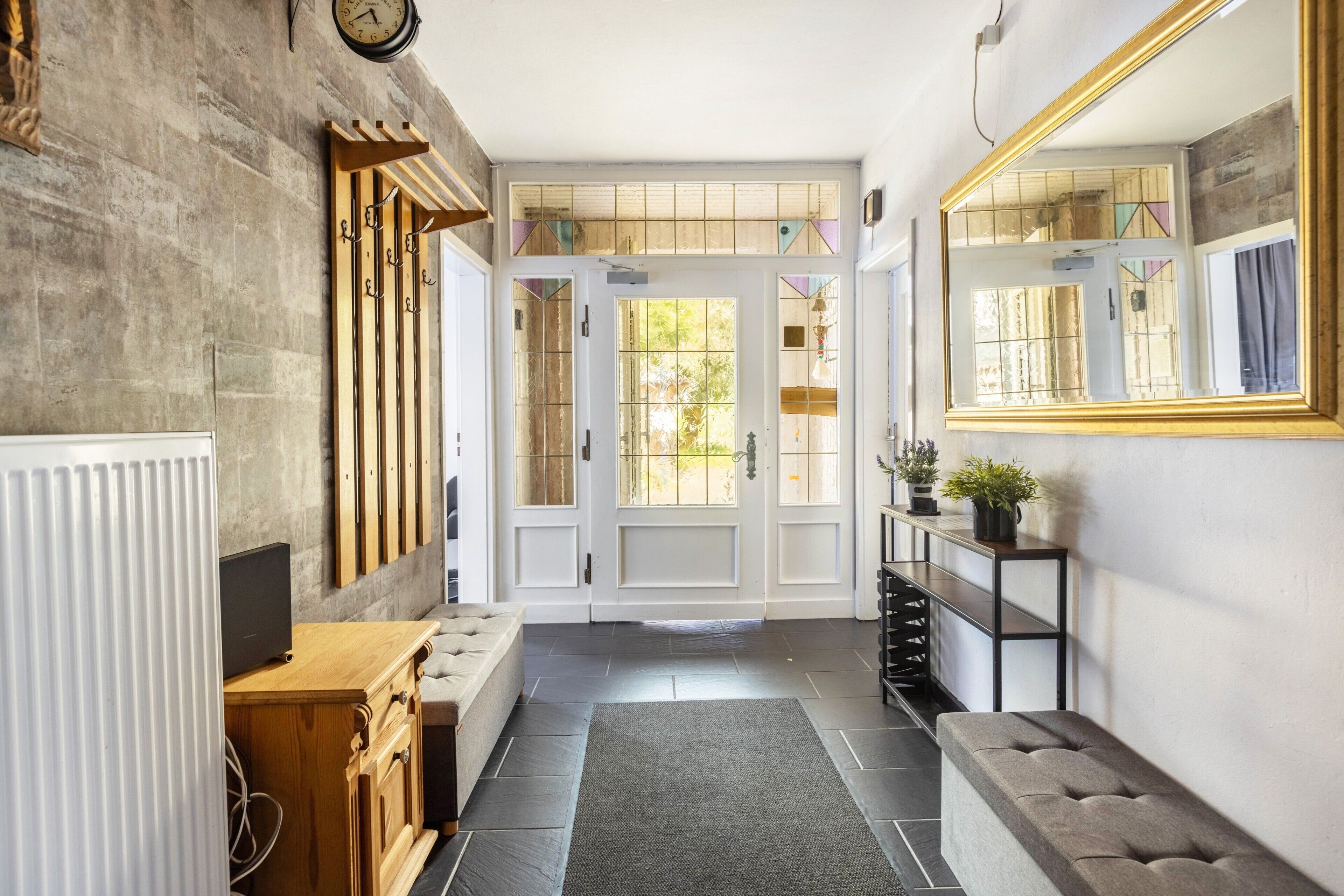 A hallway with a wooden bench, a radiator, a TV, and a mirror on the wall.