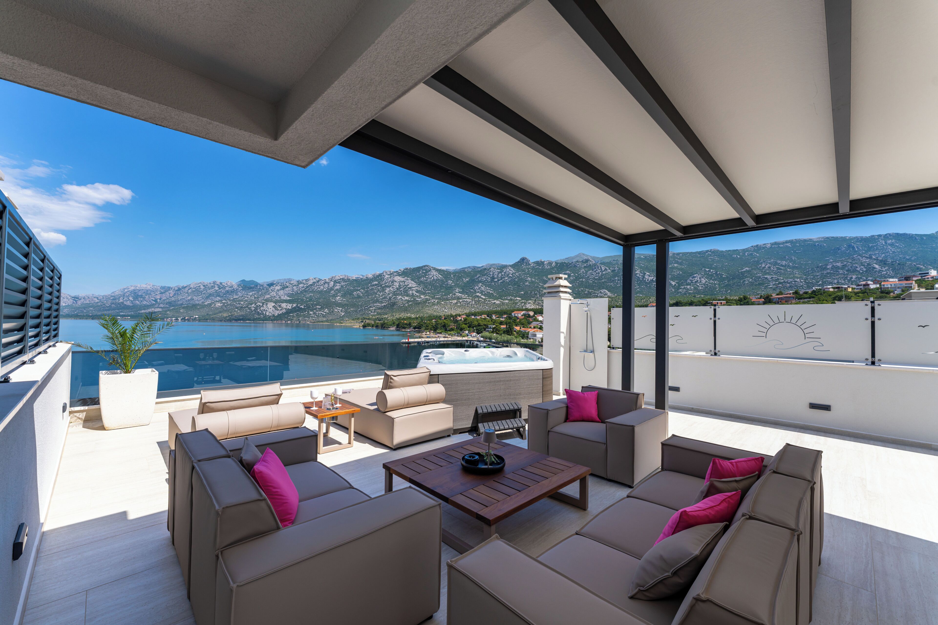 A modern outdoor living area with a view of a lake and mountains, furnished with sofas and a table.