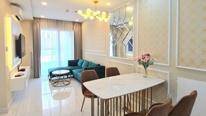 A modern living room with a dining area, a sofa, a TV, and a decorative mirror. - Terra Royal - Luxury Apartment & Hotel in Ho Chi Minh City (Thành phố Hồ Chí Minh)