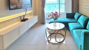 A modern living room with a flat-screen TV, a sofa, a coffee table, and a view of a cityscape through the window. - Terra Royal - Luxury Apartment & Hotel in Ho Chi Minh City (Thành phố Hồ Chí Minh)