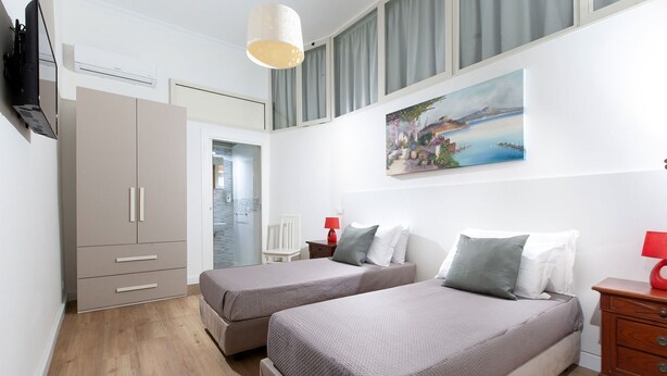 Een slaapkamer met twee bedden, een televisie, een schilderij en een kledingkast.