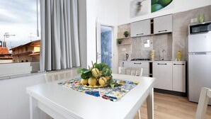 Een moderne keuken met witte kasten, een eettafel met een kleurrijke tafelkleed en een raam met gordijnen.