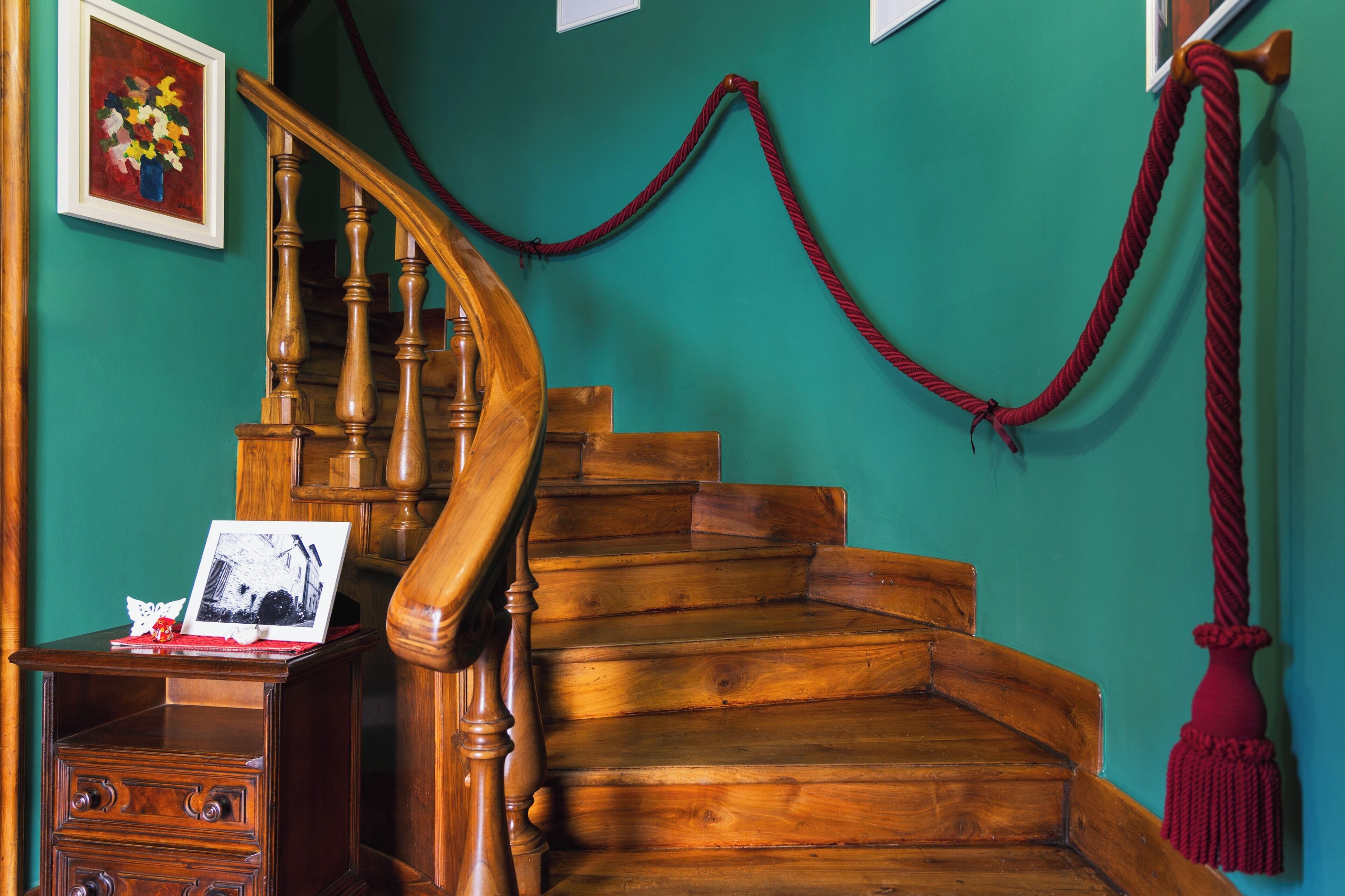A wooden staircase with a red rope barrier, a wooden desk with drawers, and a framed picture on the wall.