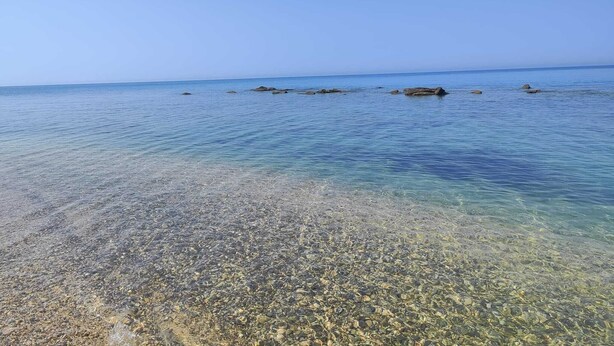 Een helder uitzicht op een kiezelstrand dat uitkomt op kalm water met verspreide rotsen.